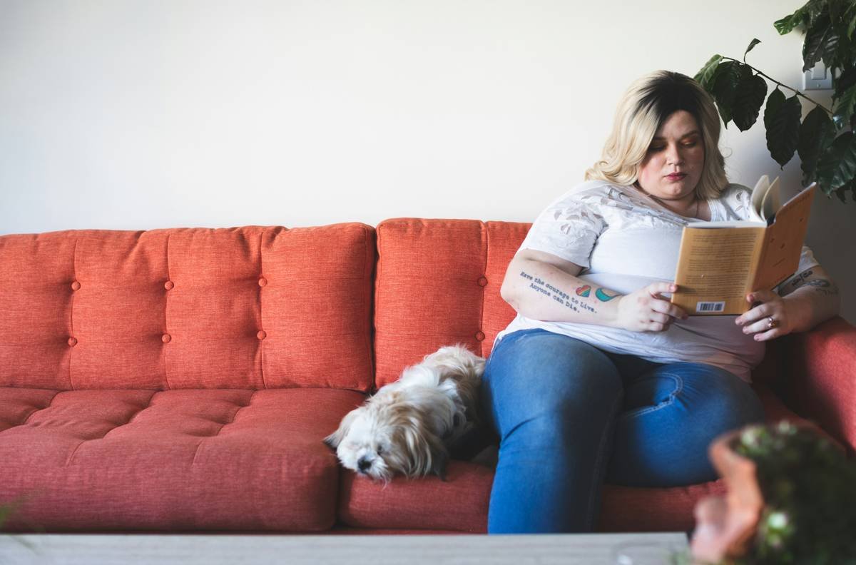White plus size woman reading on couch with dog