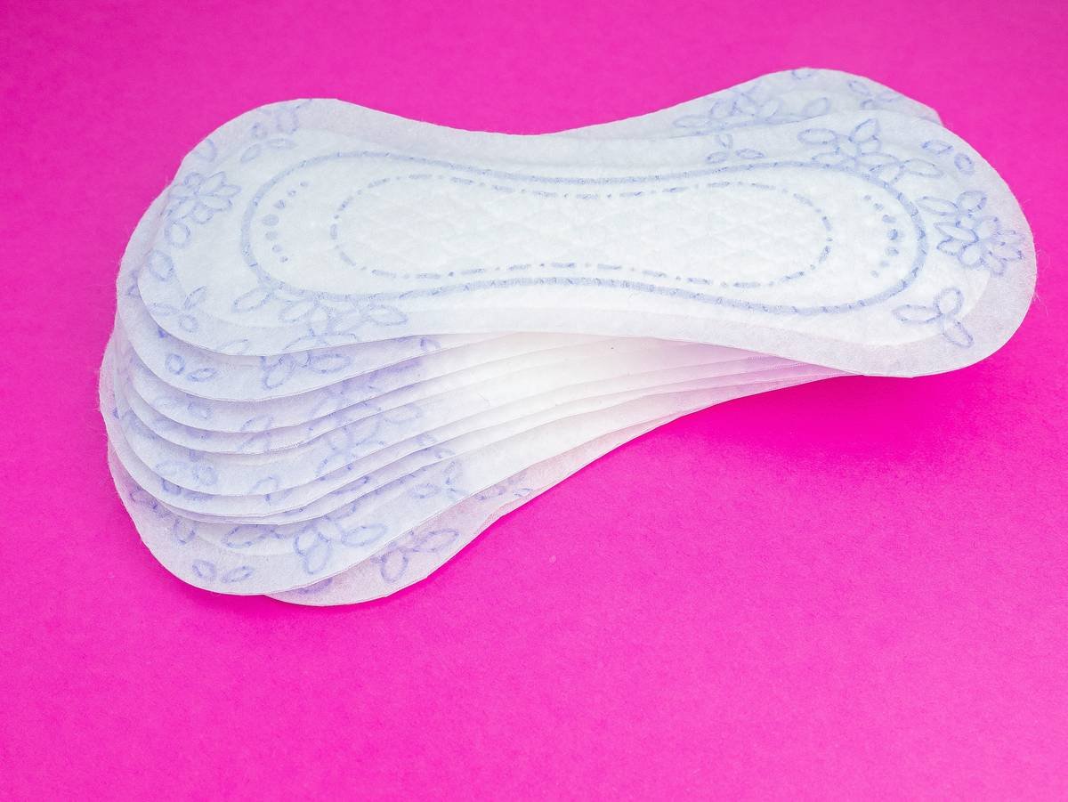 Side-by-side infographic comparing materials in conventional pads (plastic, rayon, fragrance) vs organic eco friendly pads (GOTS-certified cotton, plant-based backing, no synthetics)